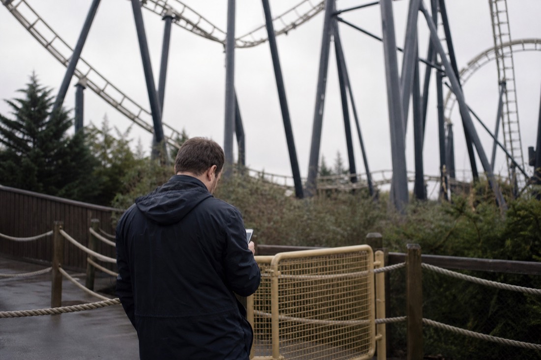 Visitor pausing at a temporarily closed ride entrance, checking a phone for the live schedule
