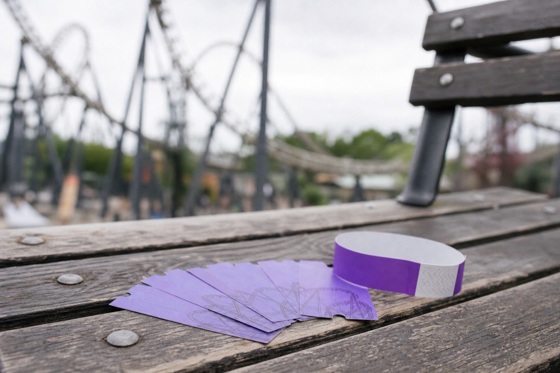 A Fuji-Q Highland day-pass wristband beside loose paper ride-ticket coupons on a wooden bench, weighing the unlimited pass against paying per ride