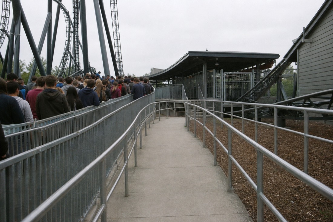 Empty priority boarding lane curving toward a coaster station while the standby queue fills the rails behind it