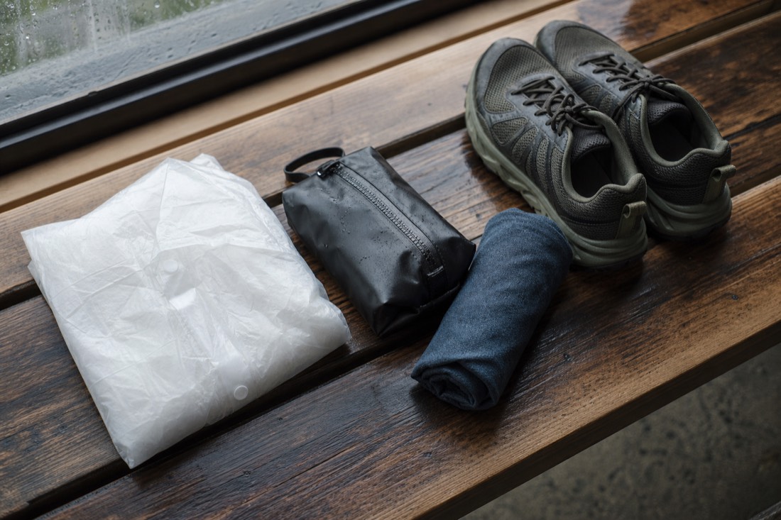 Folded rain poncho, closed grippy shoes, a zip dry pouch and a small towel laid out on a wooden bench ready for a wet theme park day